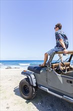 Caucasian man sitting in windshield of convertible car on beach