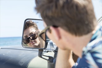 Reflection of Caucasian man in side-view mirror of car on beach