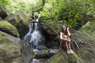 Mixed Race woman sitting on rock near waterfall