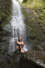 Caucasian woman sitting on rock near waterfall