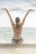 Ocean waves splashing on Caucasian woman wearing bikini