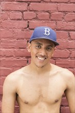 Portrait of shirtless Mixed Race man wearing hat near brick wall