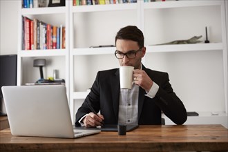 Caucasian businessman using laptop and digital tablet drinking coffee