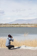Caucasian woman photographing mountains at river