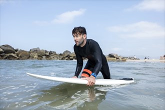 Caucasian man wading in ocean holding surfboard