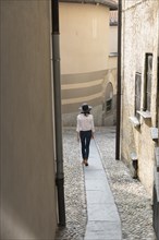 Woman wearing sun hat walking on narrow sidewalk
