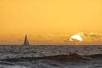Distant sailboat in ocean at sunset