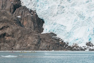 Distant people kayaking near glacier
