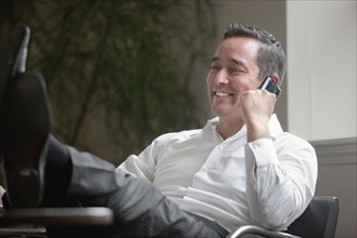 Mixed race businessman with feet on desk using cell phone