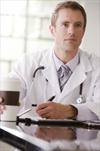 Caucasian doctor drinking coffee and writing in medical record