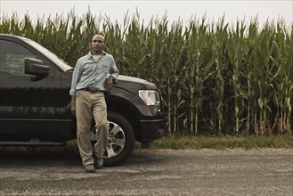 African American farmer leaning on car next to crop