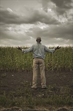 African American farmer standing in field with arms outstretched