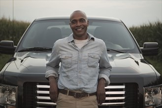 African American man leaning on hood of car