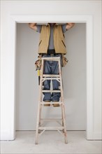 Caucasian carpenter standing on ladder in doorway