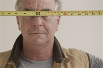Caucasian carpenter covering eyes with measuring tape