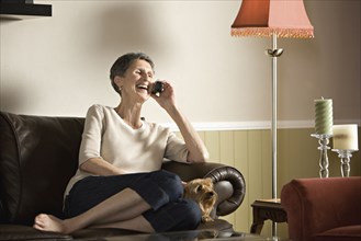 Senior woman sitting on sofa talking on telephone