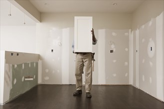 African American man holding cabinet door in unfinished room