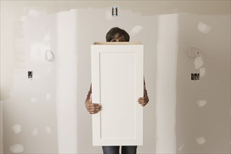 Mixed race woman holding cabinet door in unfinished room