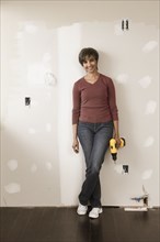 Mixed race woman holding cordless drill in unfinished room