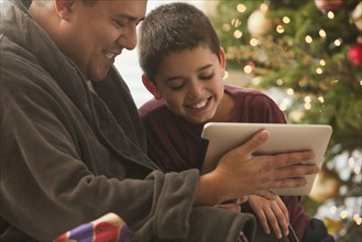 Hispanic father and son looking at digital tablet on Christmas morning