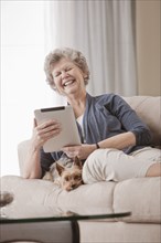 Caucasian woman sitting on sofa using digital tablet with dog