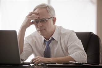 Frustrated Caucasian businessman using laptop at desk