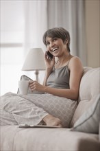 Mixed race woman on sofa talking on cell phone