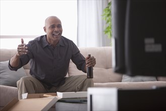 Black man drinking beer and watching television