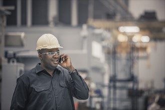 African American worker using cell phone in factory