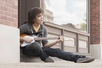 Mixed race teenager playing electric guitar and singing