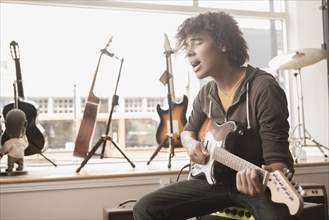 Mixed race teenager playing electric guitar and singing