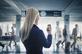 Caucasian businesswoman text messaging on cell phone in airport