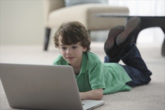 Caucasian boy laying on floor using laptop