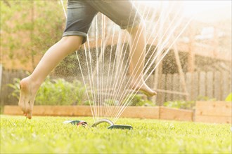 Caucasian girl running through sprinkler in backyard