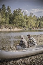 Caucasian father and son sitting in canoe on riverbed