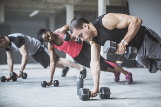 Athletes doing push-ups with dumbbells on floor
