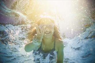 Caucasian girl swimming underwater gesturing peace sign