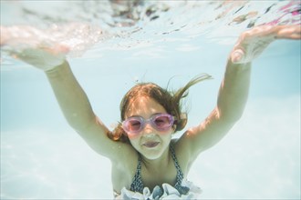 Caucasian girl swimming underwater in swimming pool