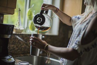 Caucasian woman pouring cup of coffee in kitchen