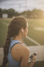Mixed race athlete listening to mp3 player on sports field
