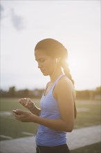 Mixed race athlete listening to mp3 player on sports field