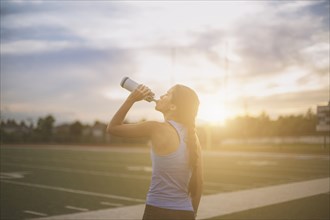 Mixed race athlete drinking water bottle on sports field