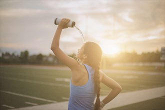 Mixed race athlete pouring water bottle on herself on sports field