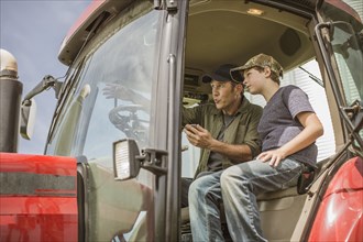 Caucasian farmer teaching son to drive tractor