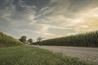 Caucasian father and son walking on dirt path by corn field