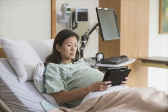 Pregnant Chinese woman in hospital room using digital tablet