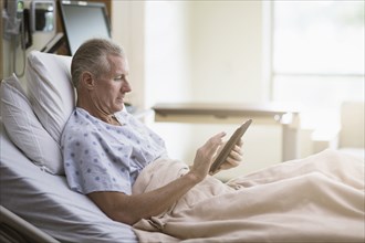 Caucasian patient using digital tablet in hotel bed
