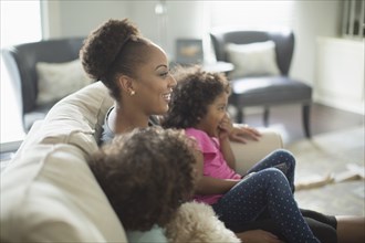 Mother and daughters watching television on sofa