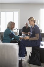 Nurse taking patient blood pressure in living room