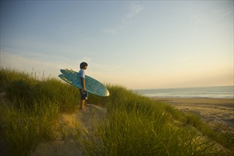 Asian boy holding surfboard at beach